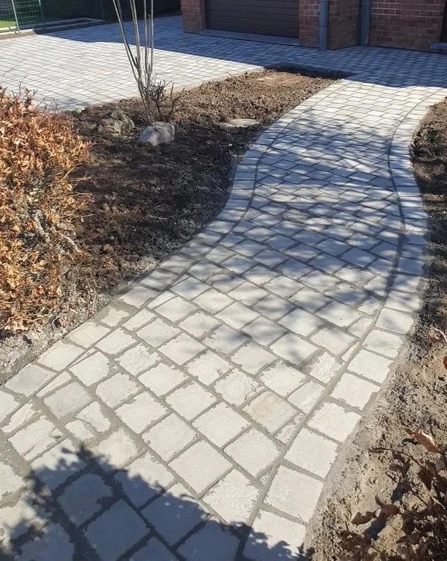Le chemin en pavés accompagne les contours du parterre.