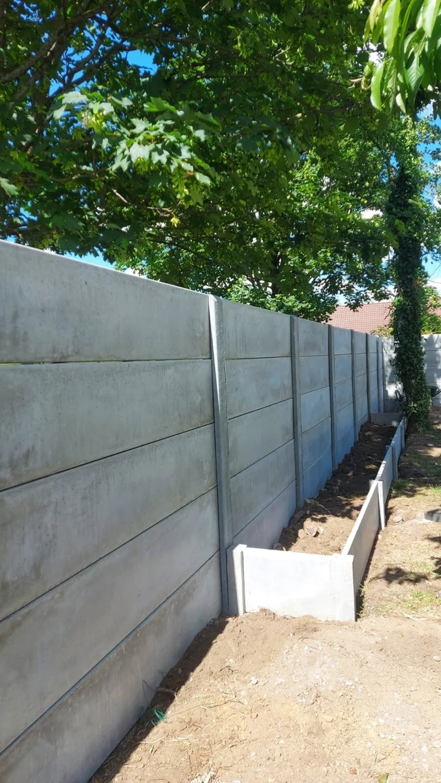 La clôture en plaques de béton crée un écran face à la cour de récréation voisine.