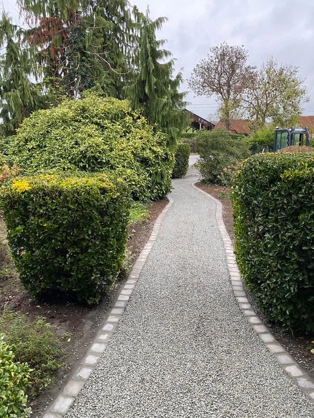 À Ghislenghien, une allée de jardin en gravier soulignée de bordures pavées.