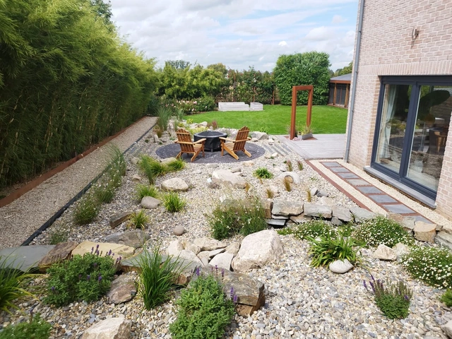 Vue d’ensemble du jardin, entre terrasse ronde, massifs et haie de bambous.