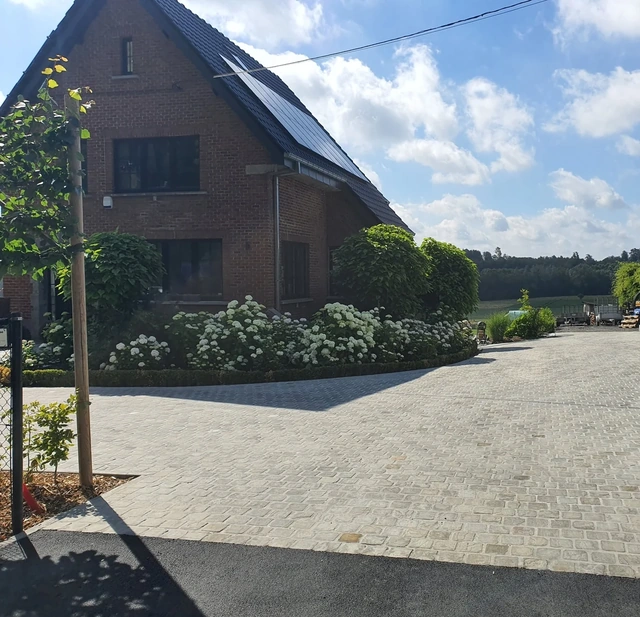 Une grande cour aménagée avec 360 m² de pavés Kandla, des arbres palissés, un parterre d’hortensias, trois catalpas et des haies, complétée par de l’asphalte en devanture.