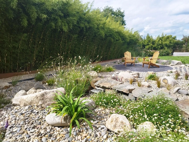 La terrasse ronde accueille deux fauteuils au milieu des pierres et des floraisons.